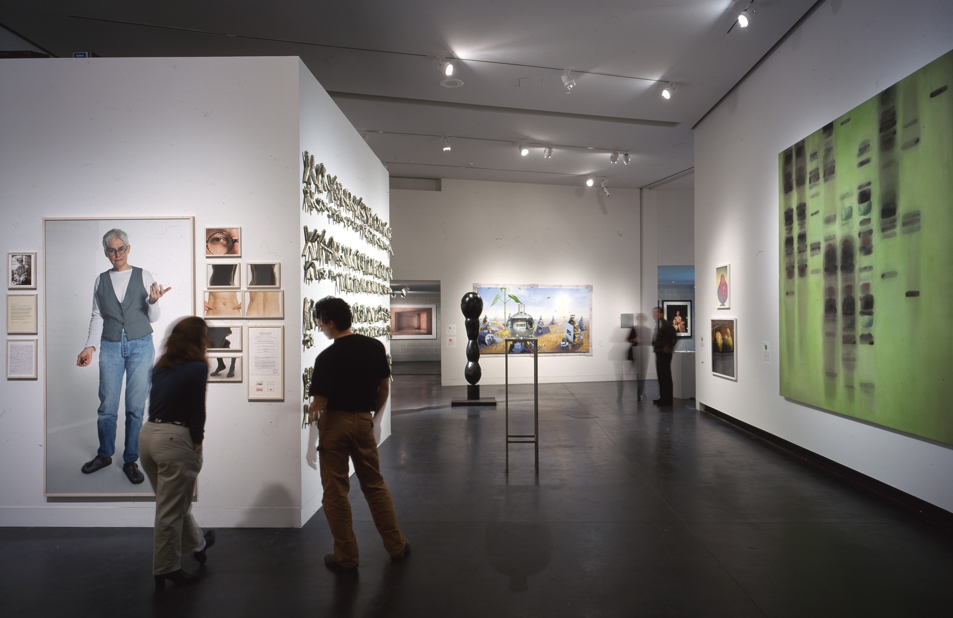 Two blurred people stand reading a wall label in a gallery next to numerous images of different sections of a human body.