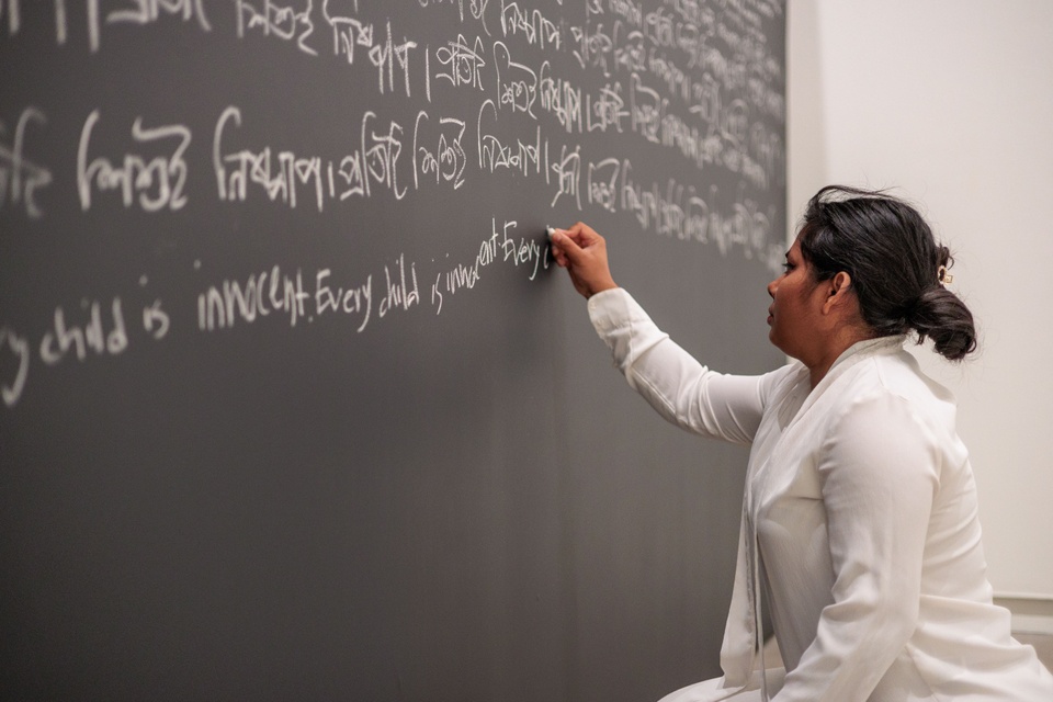 artist Tahia Farhin Haque writing with chalk on a wall in an installation piece 