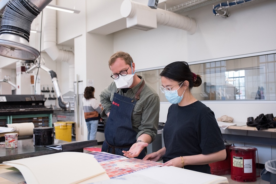 Two people look at a blue and red print on a worktable.