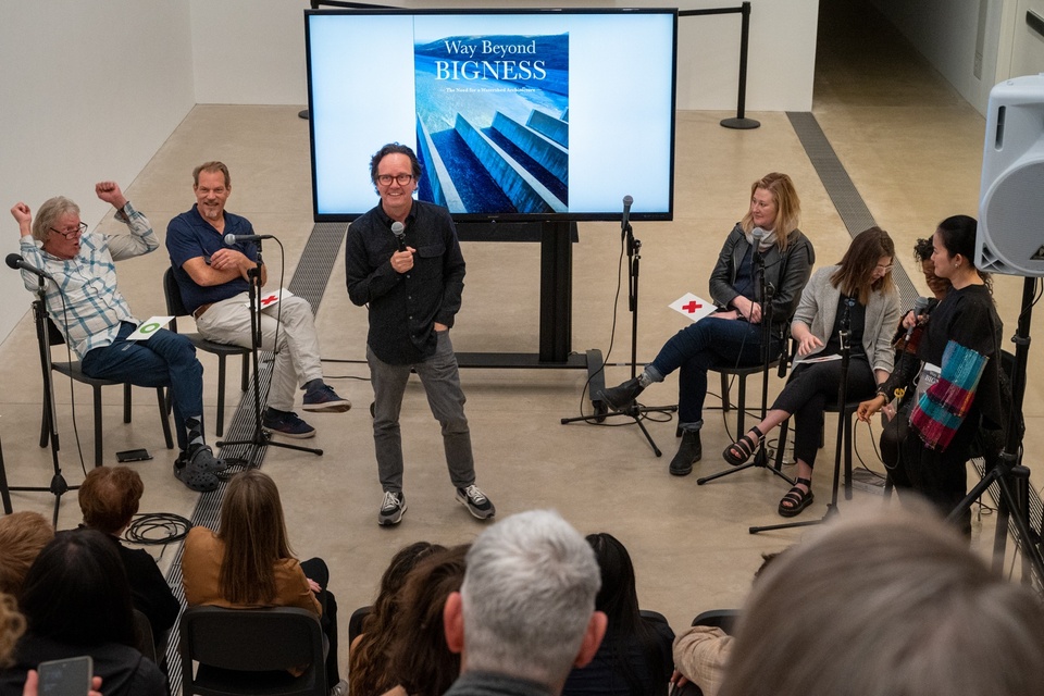 Hoeferlin stands in front of a crowd gathered on risers in the Pulitzer Arts Foundation building. Behind him is a group of panelists and a screen displaying the cover image from his book, "Way Beyond Bigness."