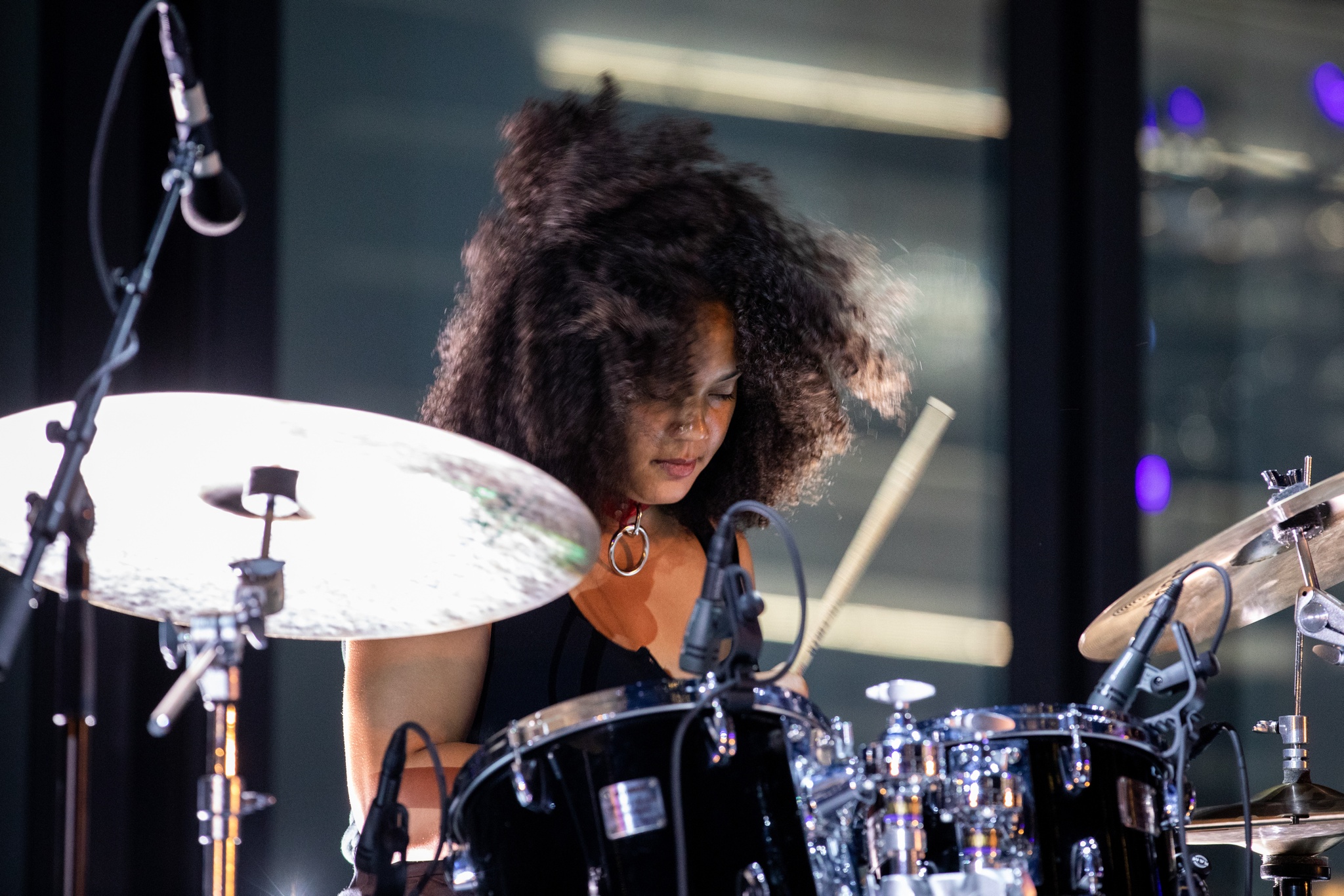 Woman playing drums on dramatically lit stage.