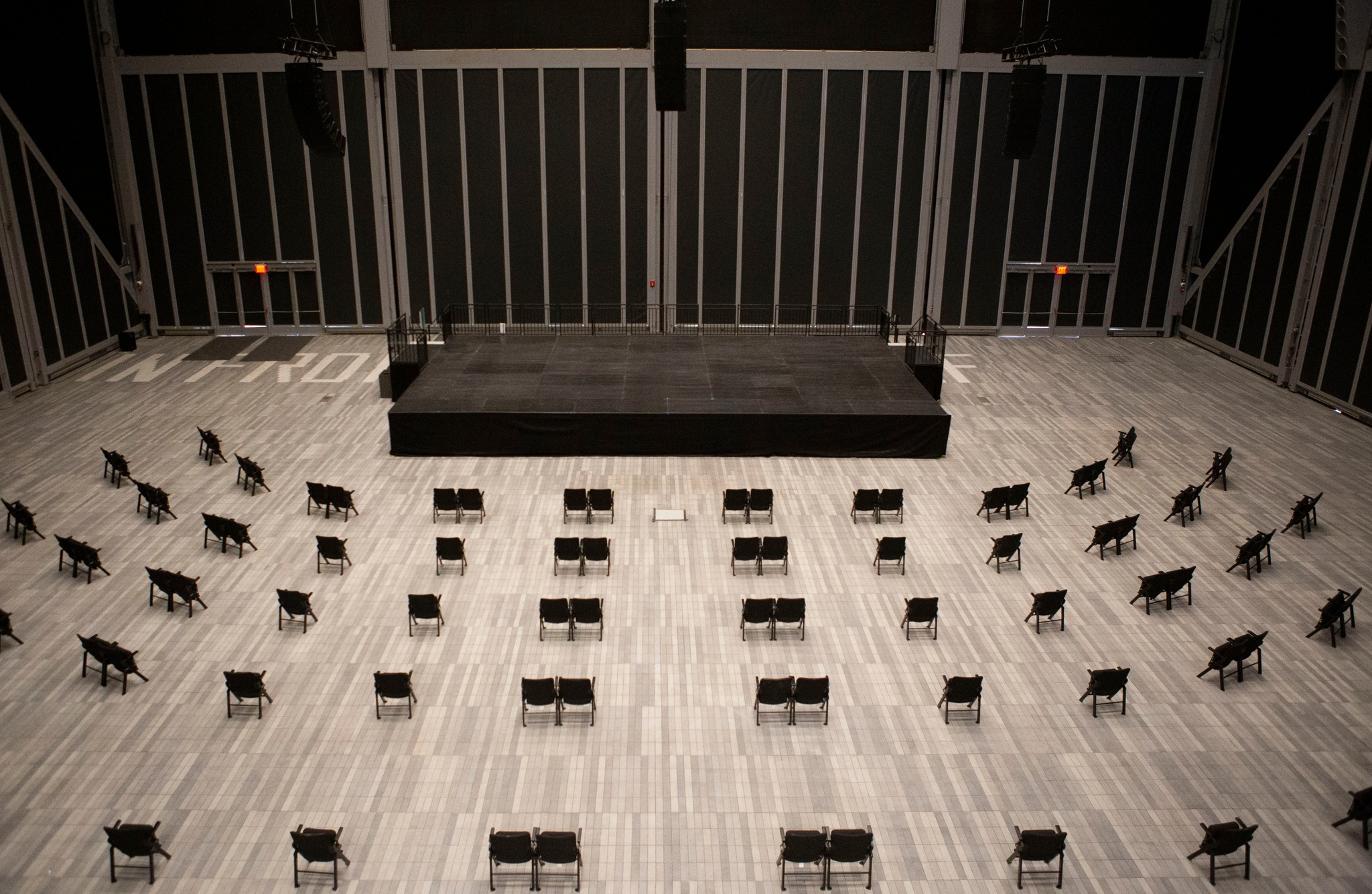The large McCourt performance space with black shades drawn over the windows and a simple black stage positioned before five rows of chairs socially distanced in pods of one or two chairs.