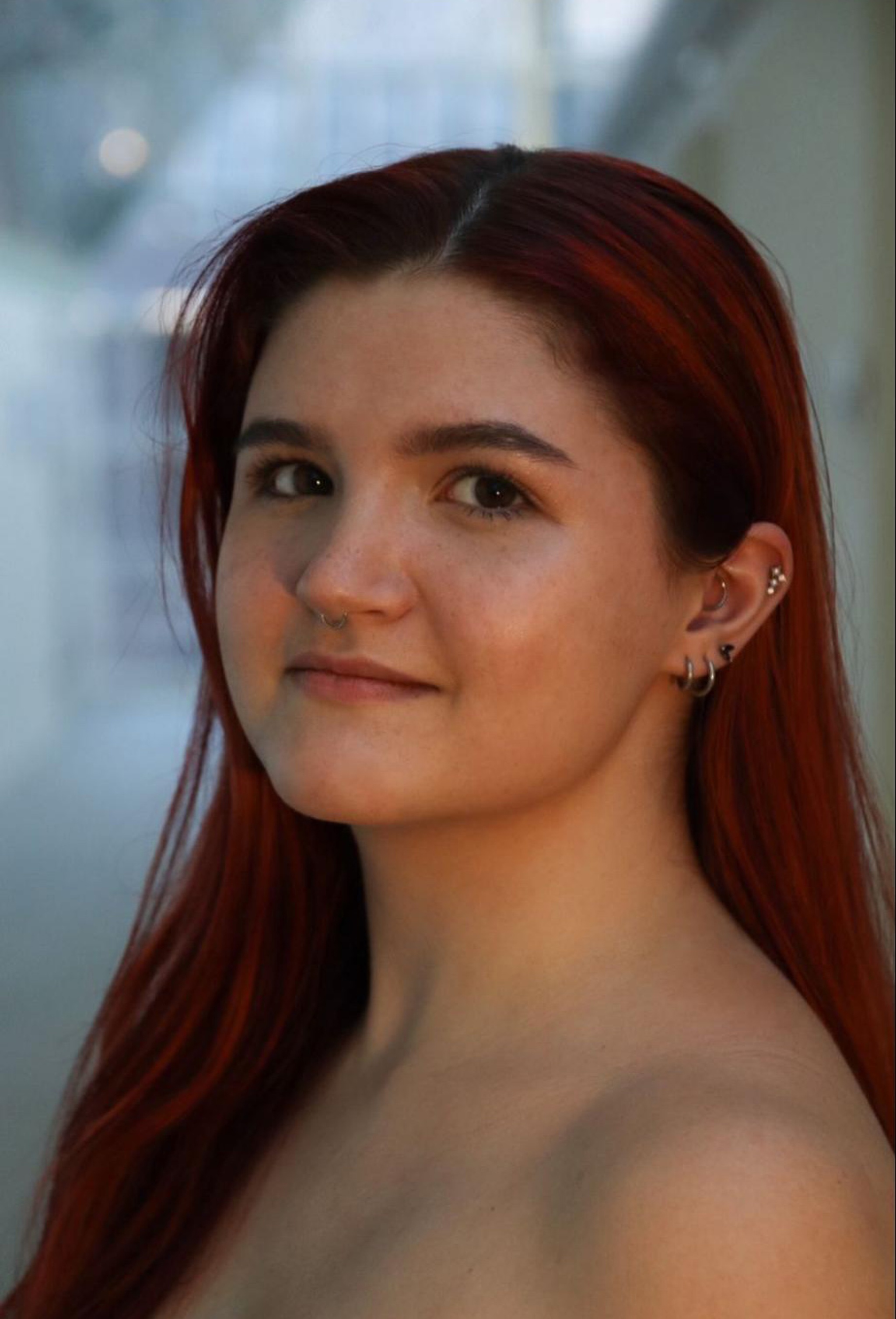 A headshot of dancer Madalyn Anderson, a white woman with long auburn hair that hangs below her bare shoulders. She turns to look at us from the side. 