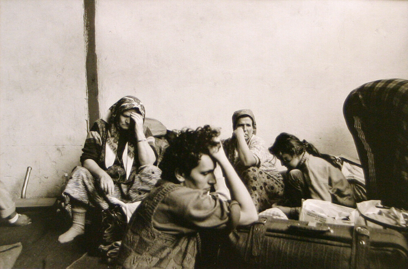 A black-and-white photograph of a group of four people sitting on the floor, two of them with their head in their hands