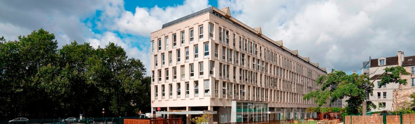 Exterior shot of building with green trees in background and blue sky with clouds