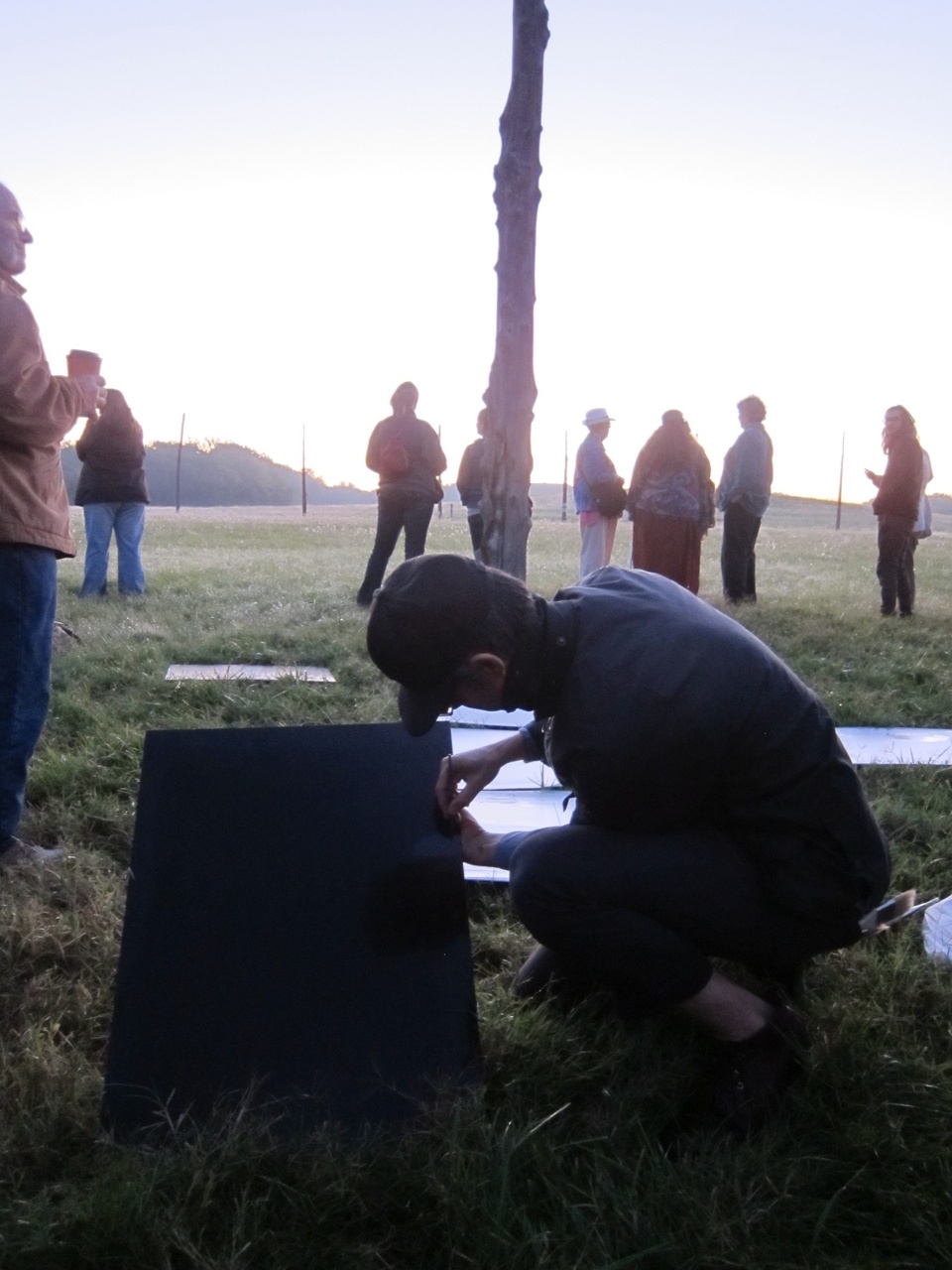 Shaun outdoors hunched over on the ground examining a large square rectangular piece of black plastic