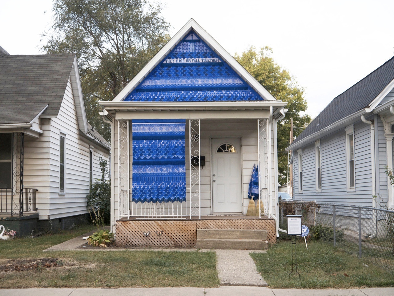 Site-specific artwork installation on the triangular roofline front plus one window area of an old house. The installation is made of a bright blue patterned fabric; at the top of the triangular portion, it says "They Rise of Fall Together."