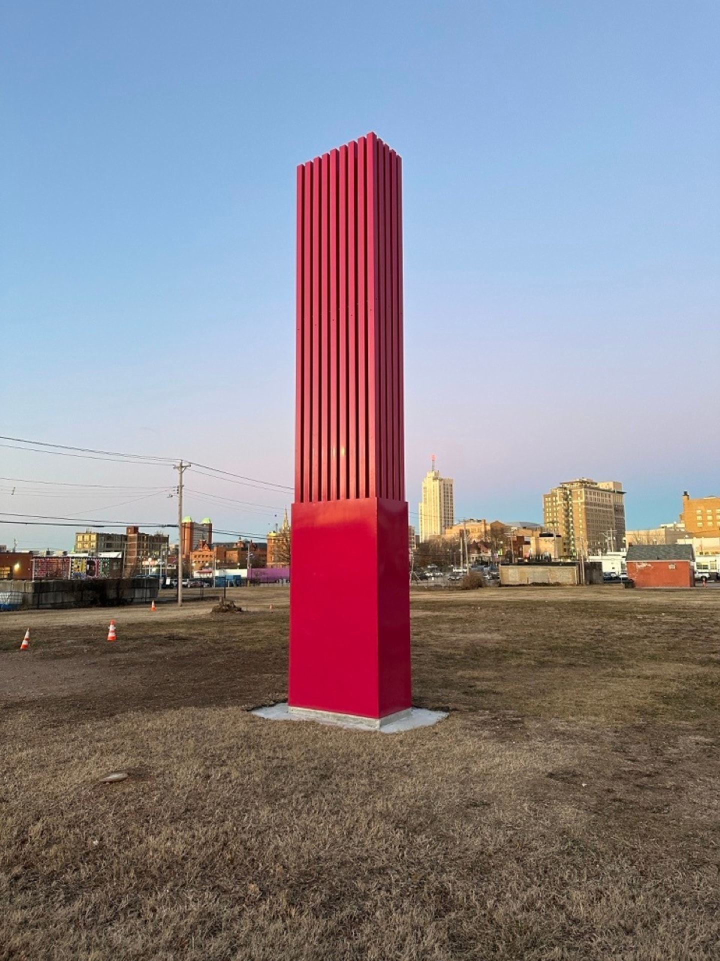 tall concrete tower painted red standing in the middle of a field with buildings in the distance