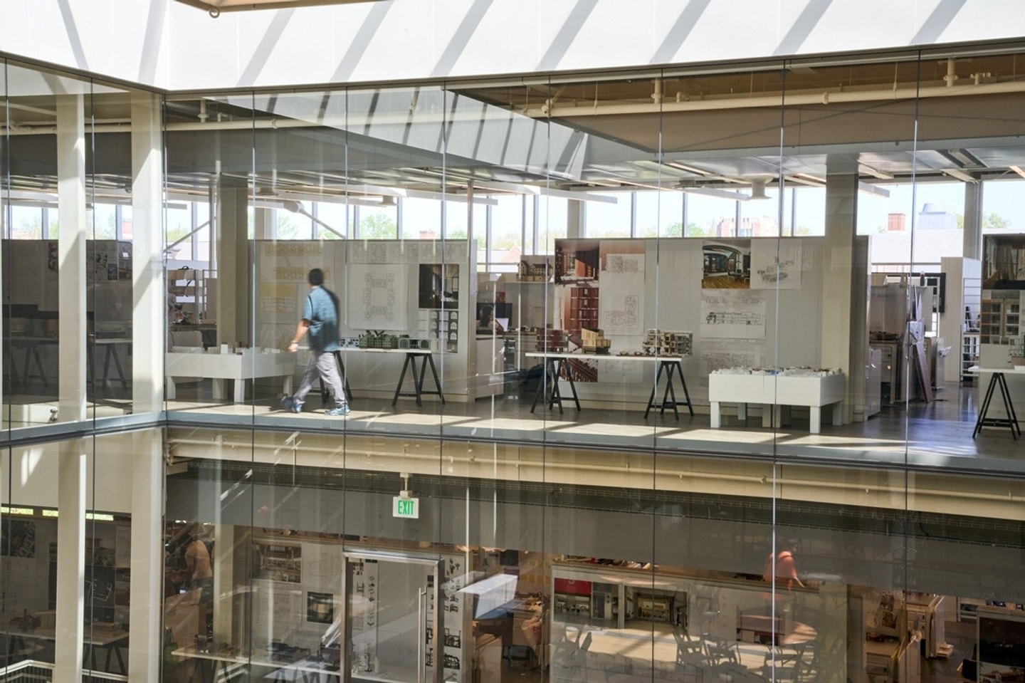 An interior view of Weil Hall showing a person walking through studios behind a glass wall.