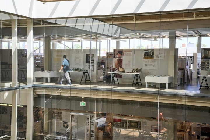 An interior view of Weil Hall showing a person walking through studios behind a glass wall.