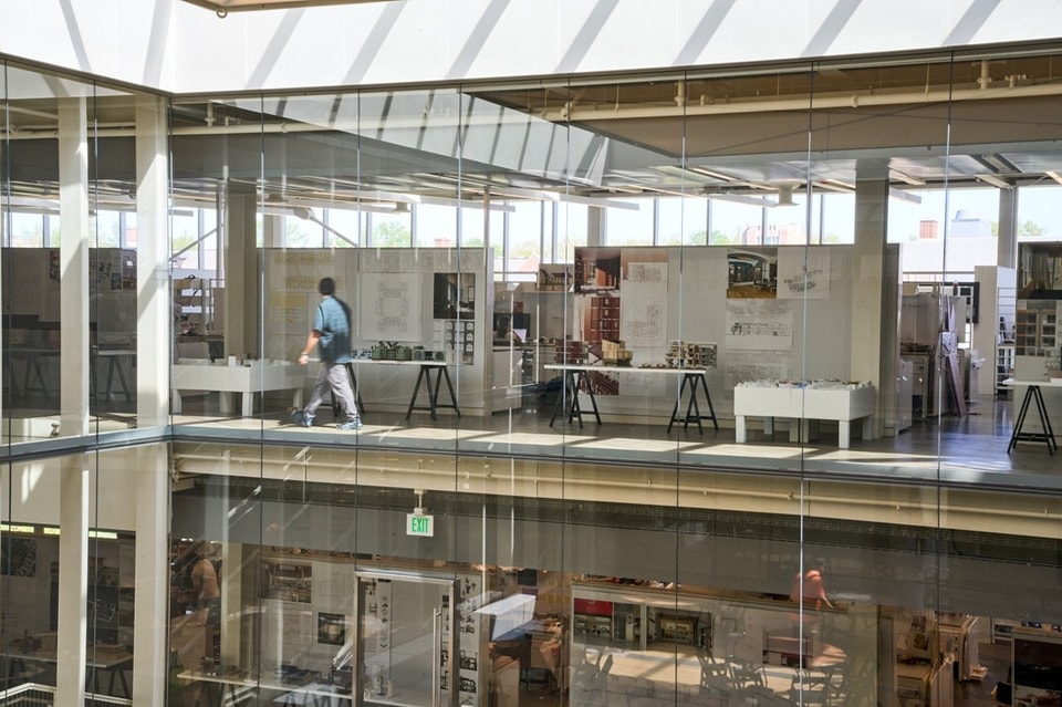 An interior view of Weil Hall showing a person walking through studios behind a glass wall.
