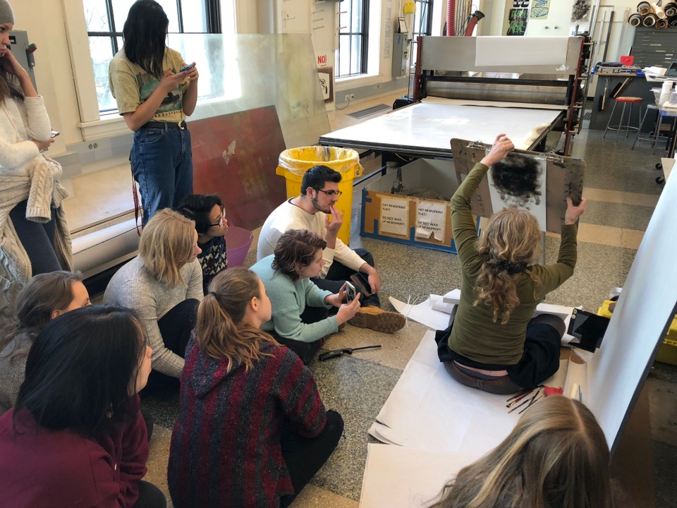 Students watching artist draw a portrait on paper with smoke from a candle.