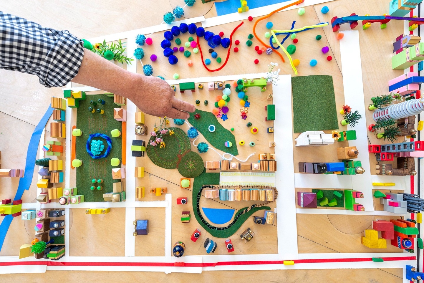 Birds eye view of a city layout made from colorful materials with a hand placing down a piece of green felt