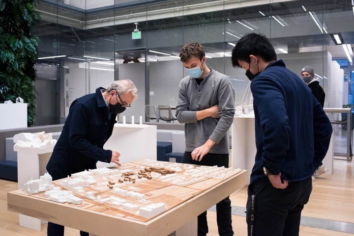 Three people stand over a model of a framework plan of a neighborhood.