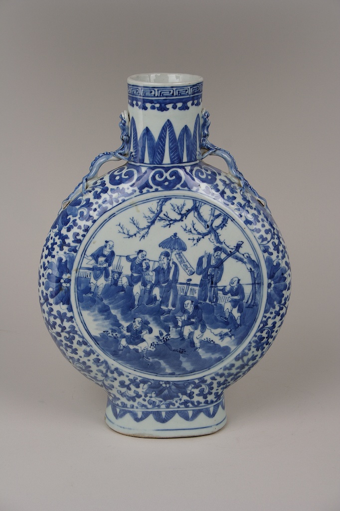 An ornate porcelain vase painted in a floral motif depicts a scene of seven men together under a tree.