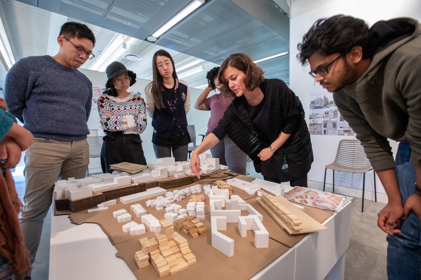 Group of people stand around a physical model of a city block on a plinth discussing.