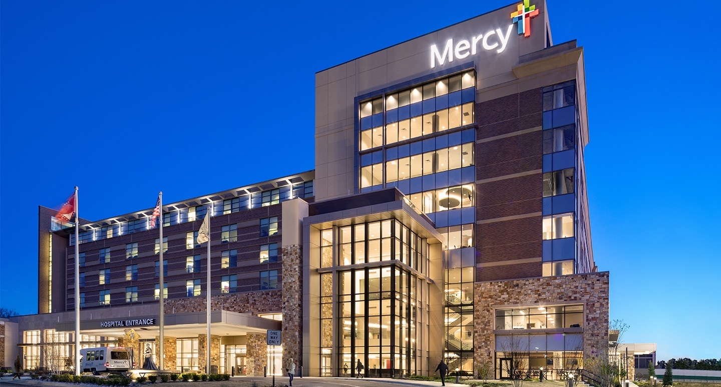 Photo of the exterior facade of a Mercy medical center at dusk, lit up from the inside.