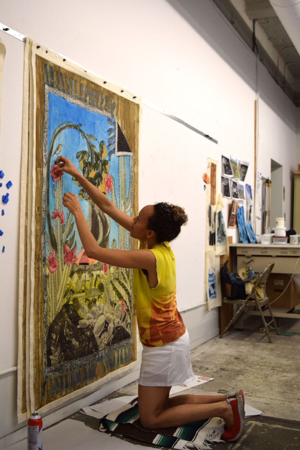 Paula adding a flower cutout detail to her large blue and green cactus print hanging on the wall 