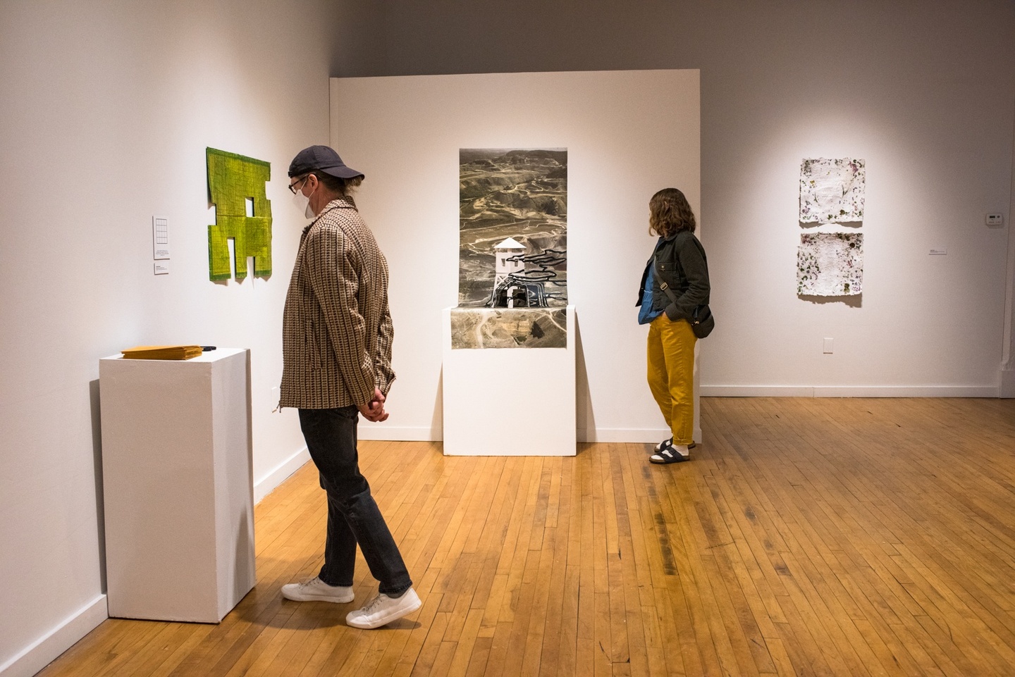 Two people in a gallery look at different artworks set on plinths.
