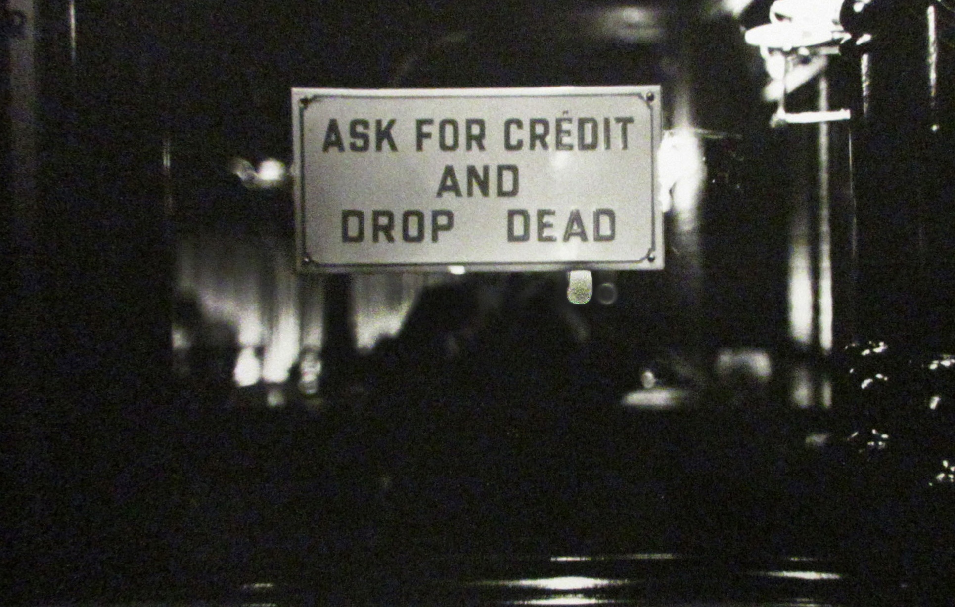 Black and white photograph of sign that reads “ASK FOR CREDIT AND DROP DEAD”