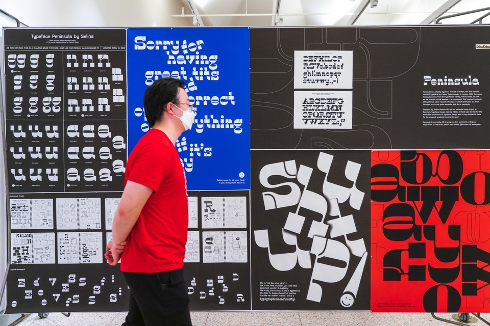 Person walks in front of a display wall of poster-sized type samples in black, red, and blue.
