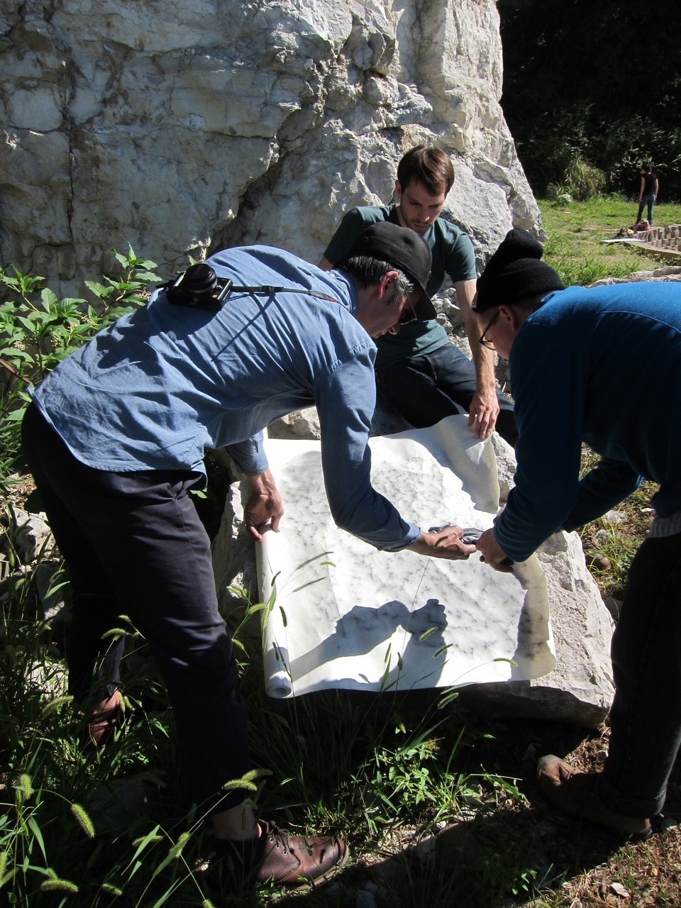 Shaun and two others hunched over examining a large piece of white paper pressed against a large rock