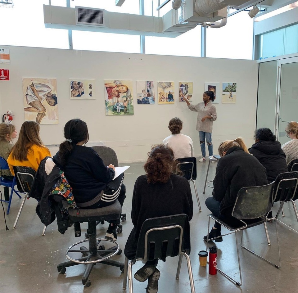 A student presents her paintings on display on a white wall in front of the class