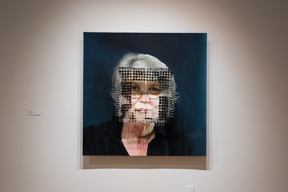 Painting of an older woman's face framed by actual charred glass pipes.