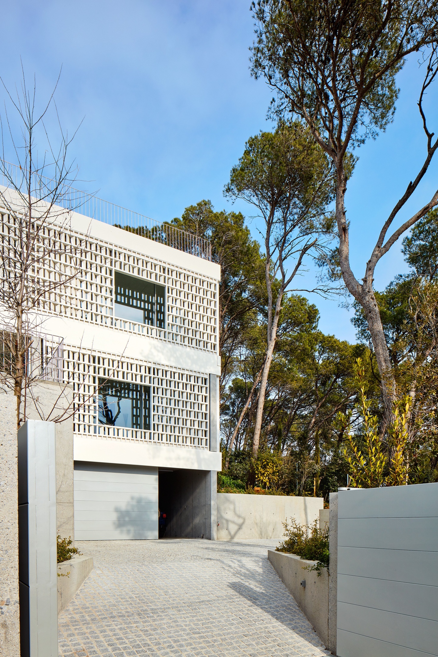 Entrance view of a house with lattice-styled walls that we can see through. There are two large windows on the two higher floors and a garage door on the ground floor