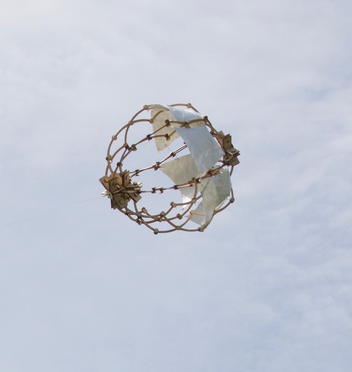 Spherical structure flying in the sky, built from thicker gold wire-like structures with connectors plus a couple of white pieces of fabric.
