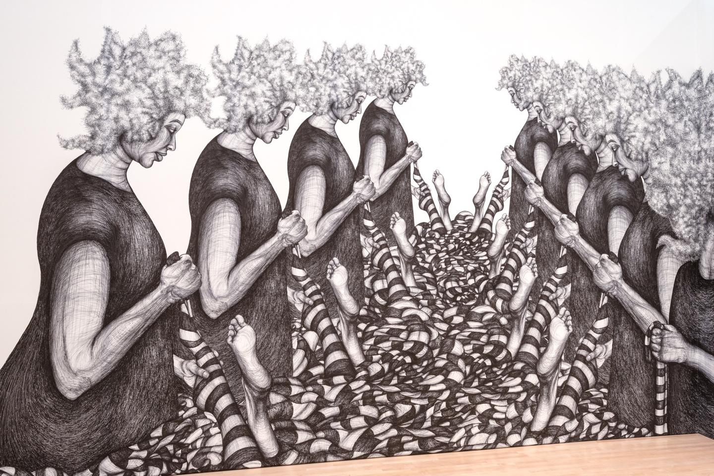 Larger than life ballpoint drawing of 8 figures in dark clothing pulling striped socks off disembodied feet in front of a pile of similar socks