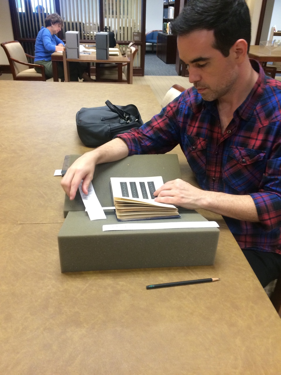 Artist Dario Robleto at the medical library examining a small book with black bars and faint white lines through them