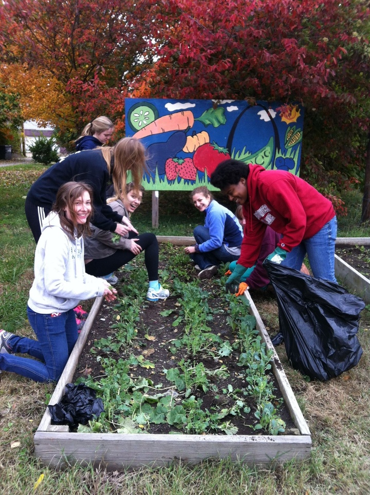 Students planting a raised bed garden in front of a mural.