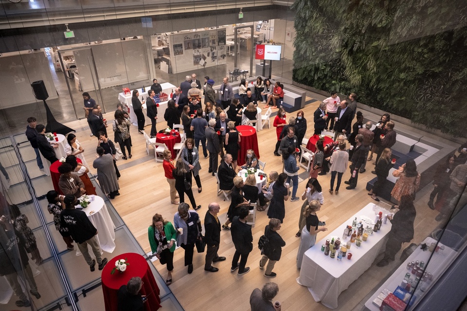 Overhead view looking down into Kuehner Court in Weil Hall. A crowd of people mill around cocktail tables with red and white tablecloths.