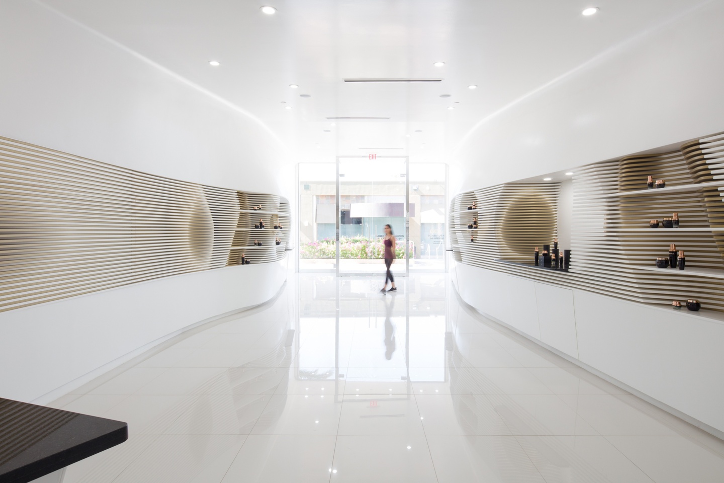 Interior perspective of a glossy white hallway with a window at the end. The walls have inset shelves with smooth divots, like a cave wall.