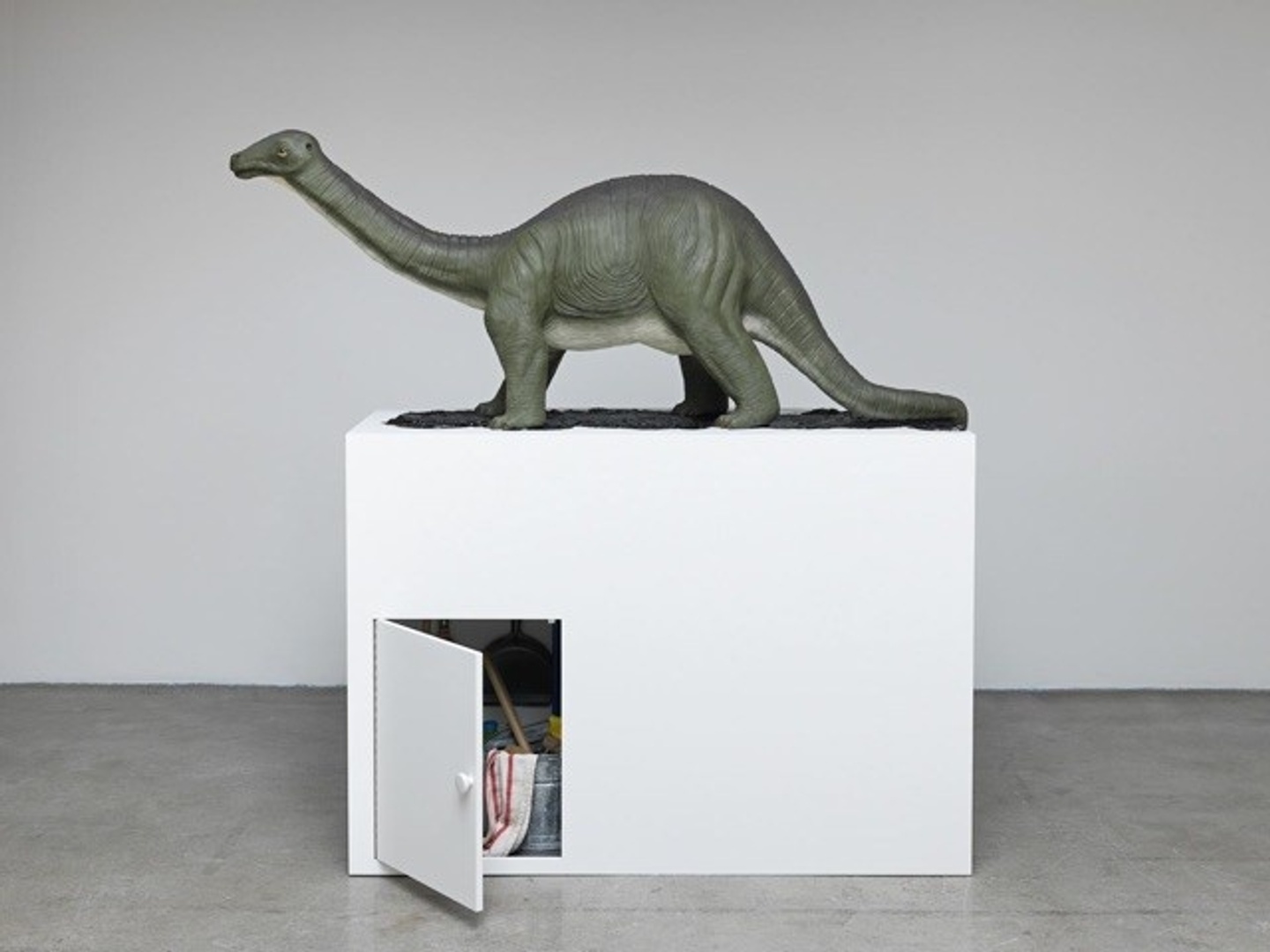 sculpture of dinosaur on top of a white box with a small door open on the bottom left