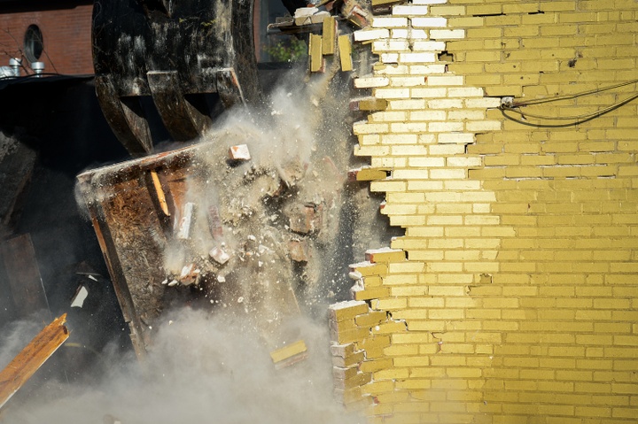 Heavy machinery breaks through a wall of bricks, painted gold. 