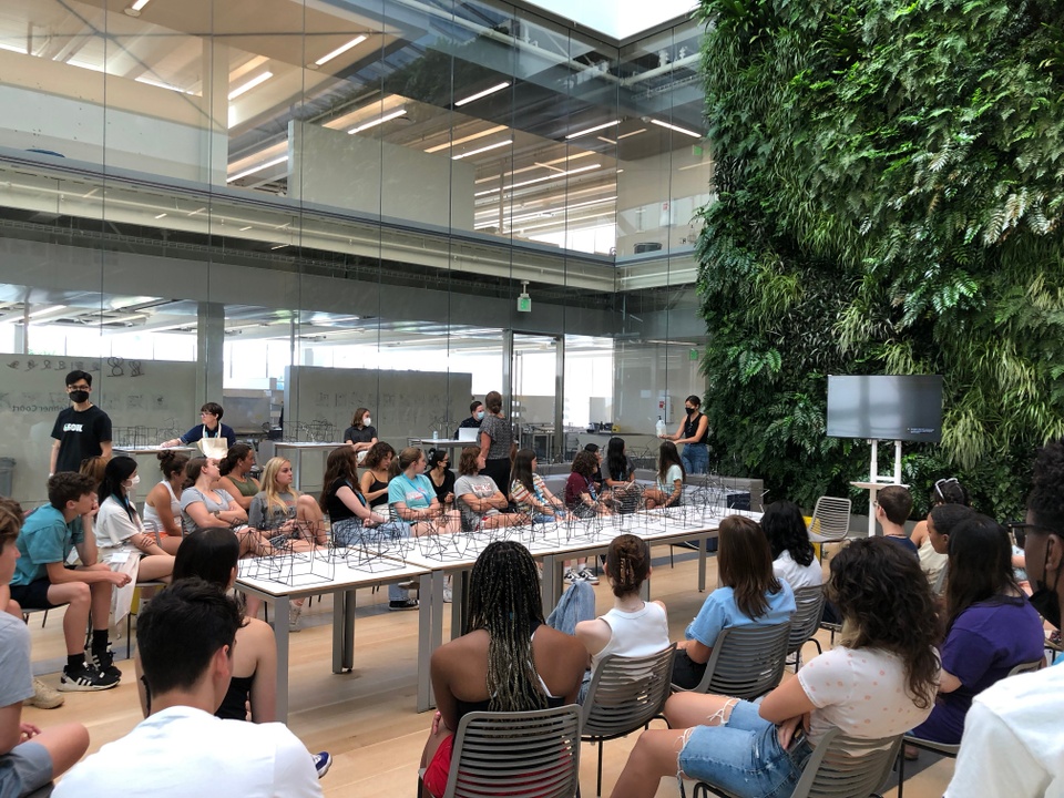 Students sit in Kuehner Court with their wire models on a long table in the middle of a room