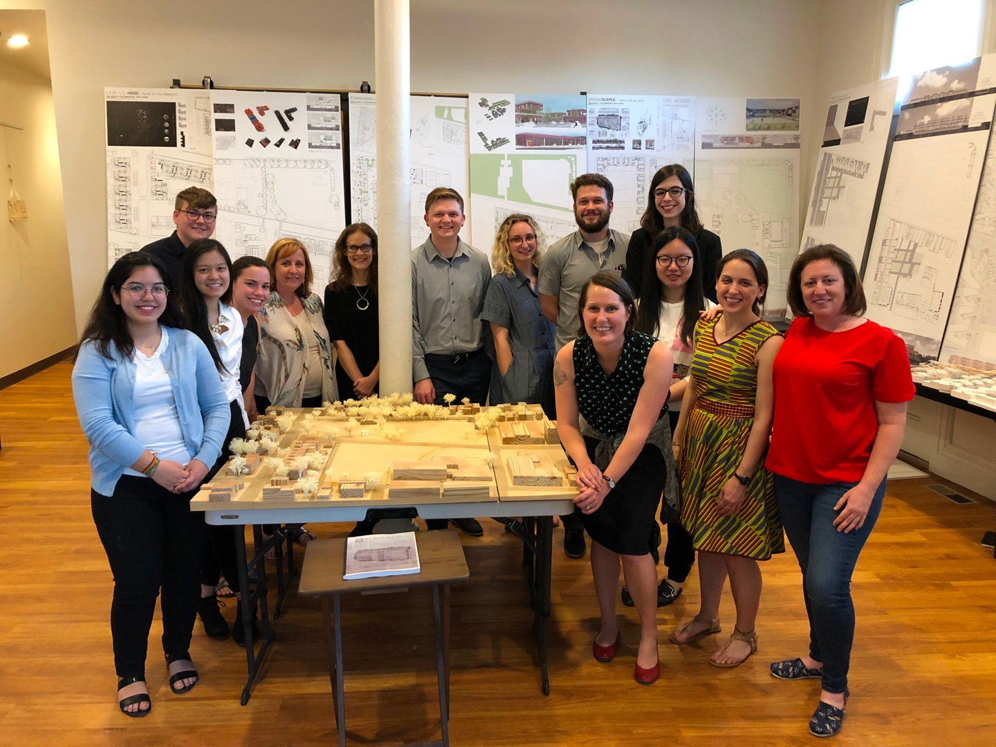 A group of people stand around a table with a model on it, surrounded by boards.