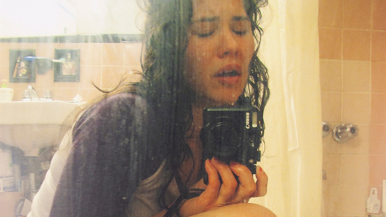 A crying woman, Laurel Nakadate, takes a selfie in a dirty mirror.