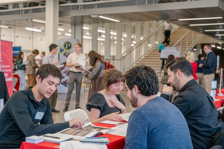 Students meet and share portfolios with two architects at a career fair table.