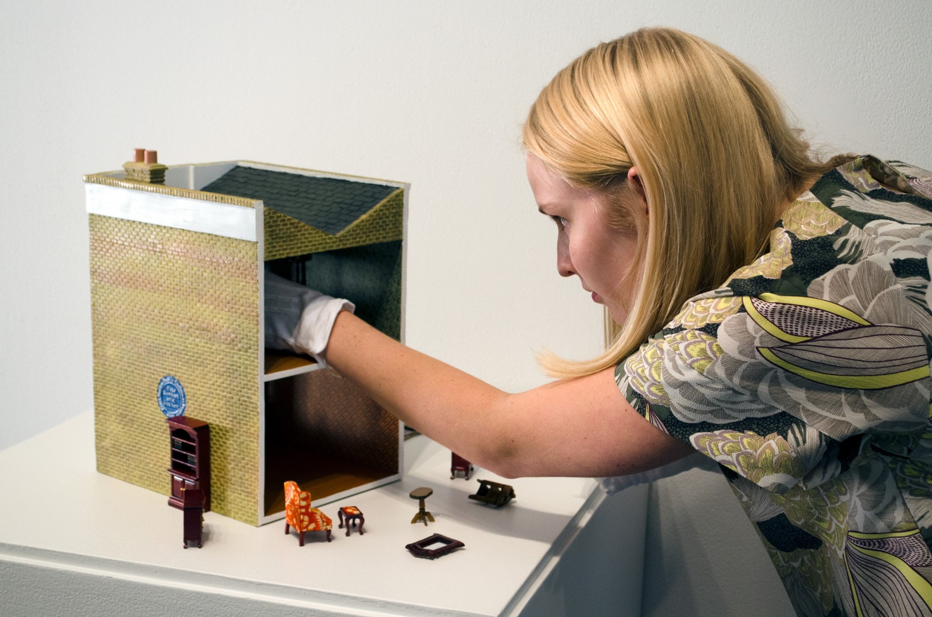 A woman installs tiny furniture into an artwork that looks like a dollhouse.