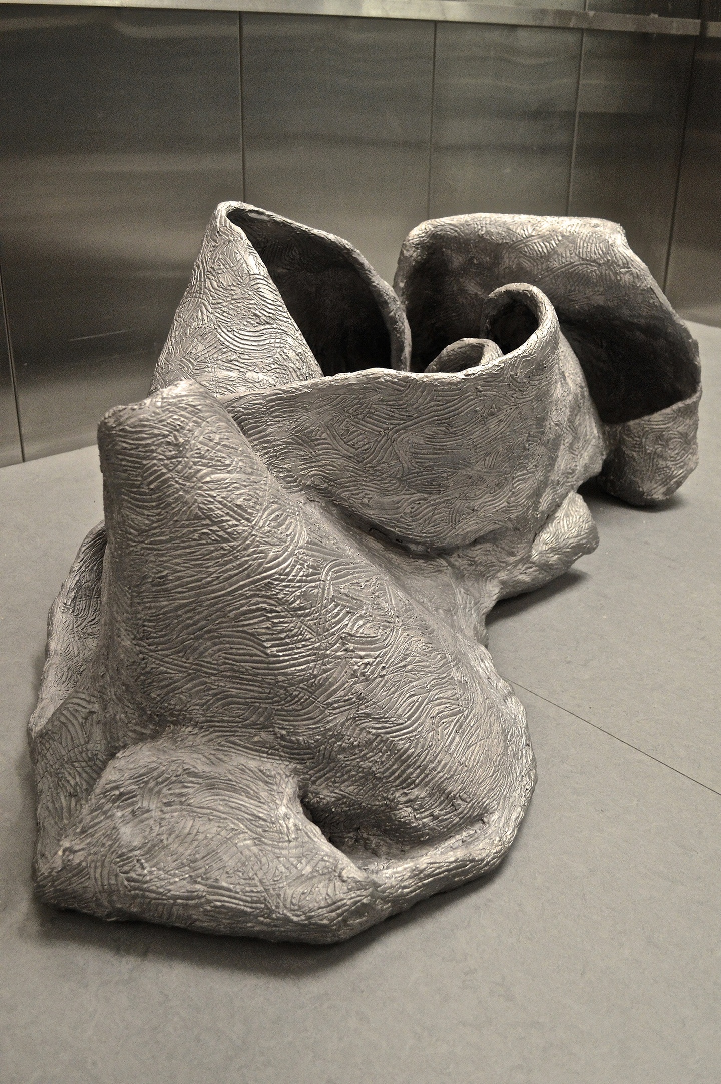 Ceramic sculpture of a long, wide sheet of clay imprinted with scratched linework that has been folded in on itself. The piece is photographed in a freight elevator.