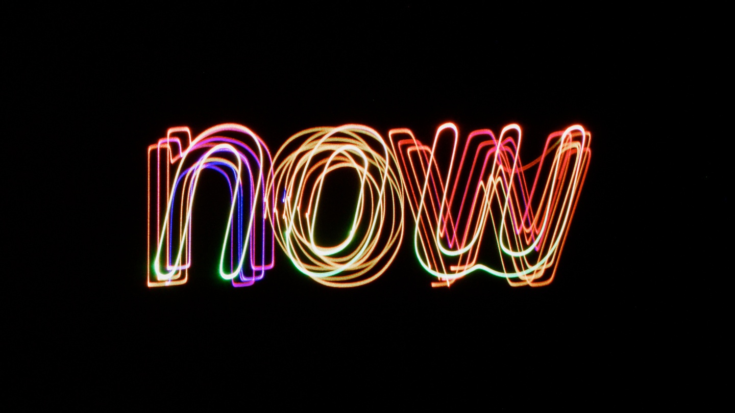 The word "now" in colorful laser lights on a black background