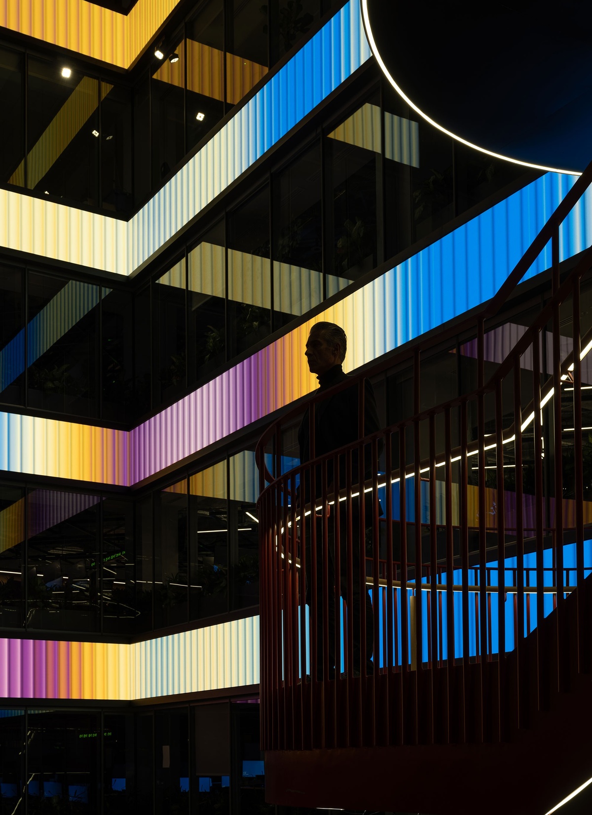 Person overlooking atrium space with four rows of horizontal LED screens behind him, lit with a yellow, purple, blue and white gradient