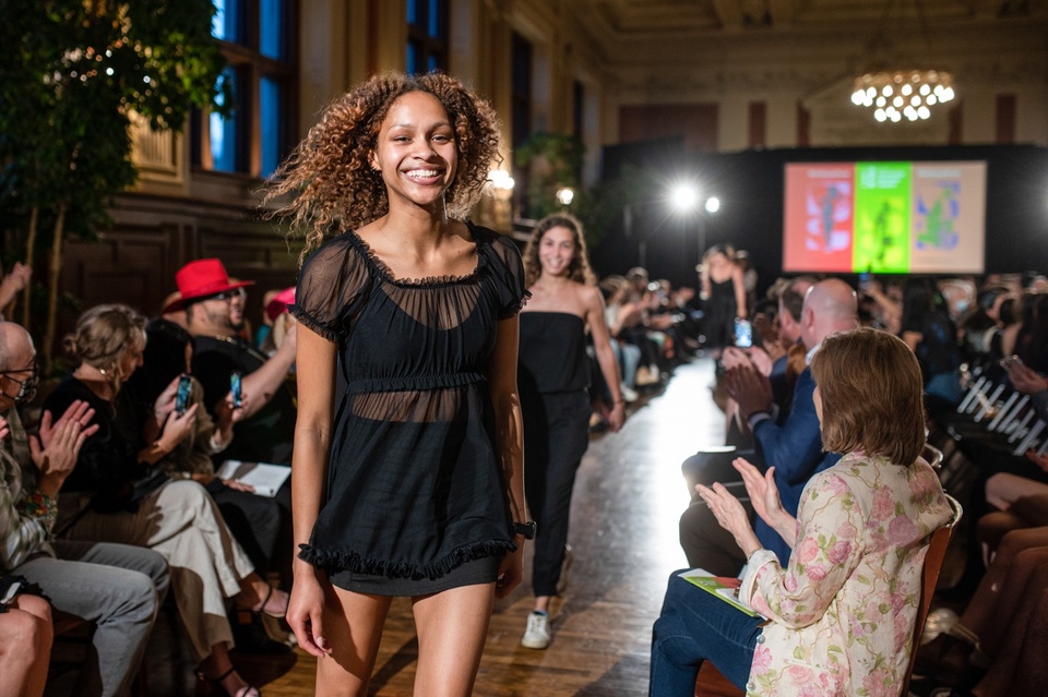 A model smiles for the camera on a runway in a black mesh dress