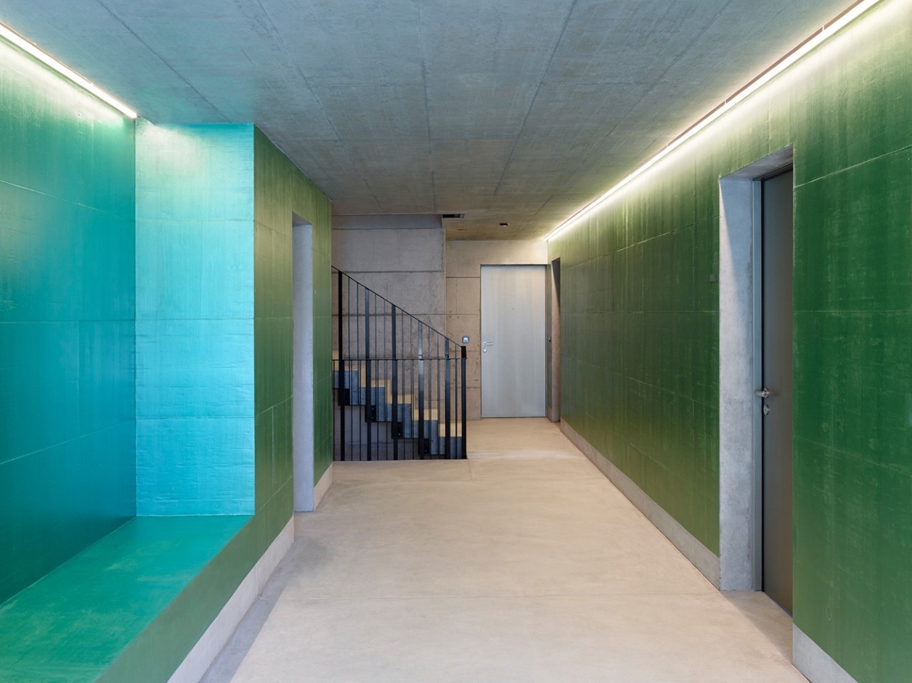 Concrete hallway and stairwell with iridescent green wall paint and recessed lighting.