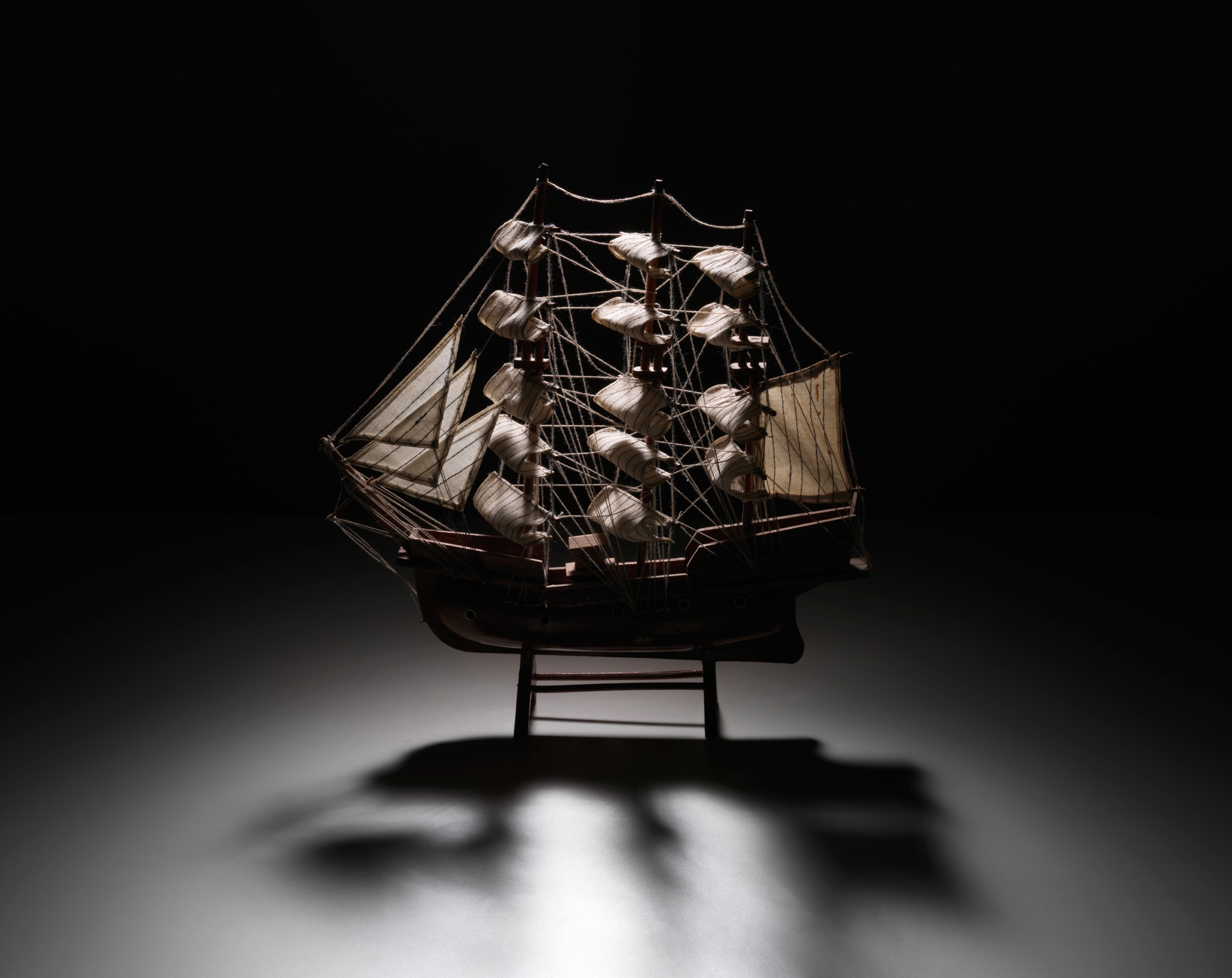 A dramatically lit model of a 17th-century ship against a black background
