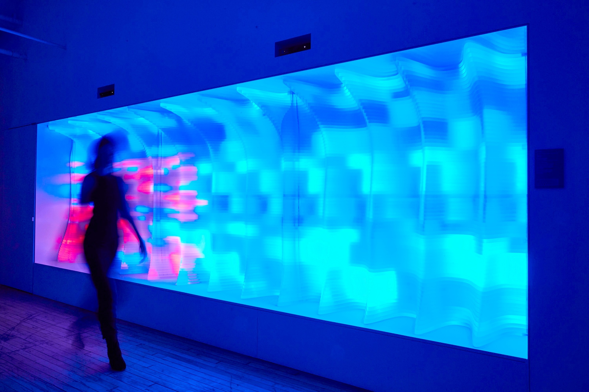 A blurred person walking past The Passage, which glows pink and blue in its artistic visualisation