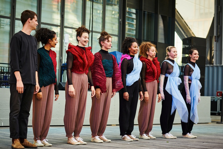 Eight dancers on an outdoor stage standing side by side